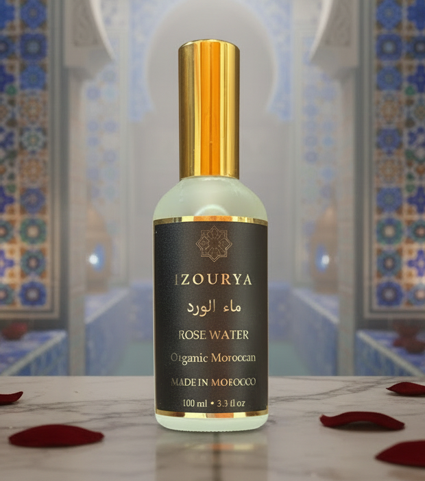 A bottle of IZOURYA Organic Moroccan Rose Water, featuring a dark brown label with gold lettering and a shiny gold cap, set against a plain white background.