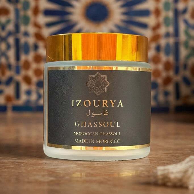 A jar of IZOURYA Ghassoul Moroccan clay powder with a black label and metallic gold cap, set against a plain white background.