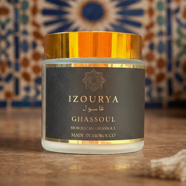 A jar of IZOURYA Ghassoul Moroccan clay powder with a black label and metallic gold cap, set against a plain white background.