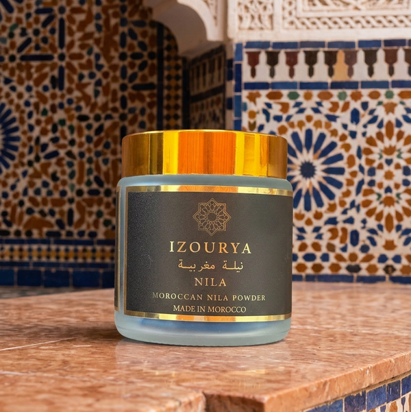 A jar of IZOURYA Moroccan Nila Powder with a metallic gold cap and a dark brown label featuring gold lettering, set against a plain white background.